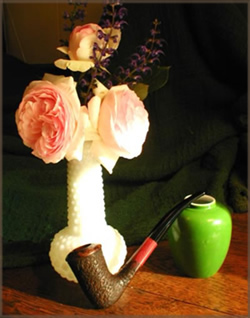 Photo of a vase with two heirloom roses and a pipe.